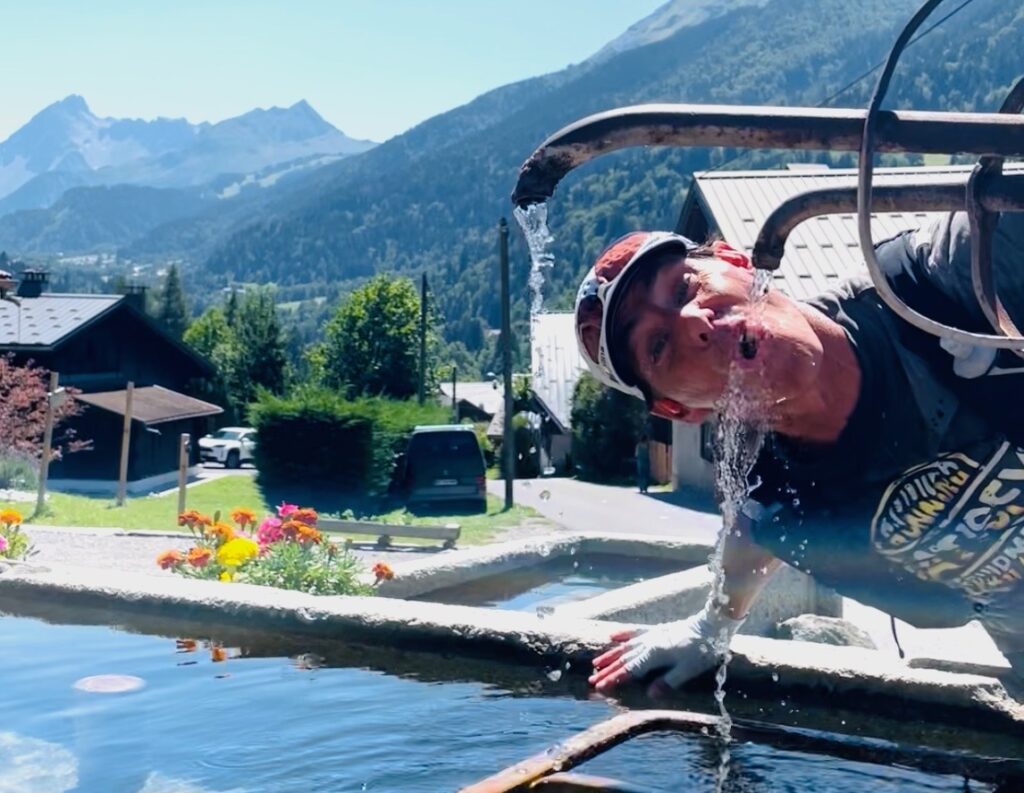 a man drinking water out of a fountain on the tmb trail